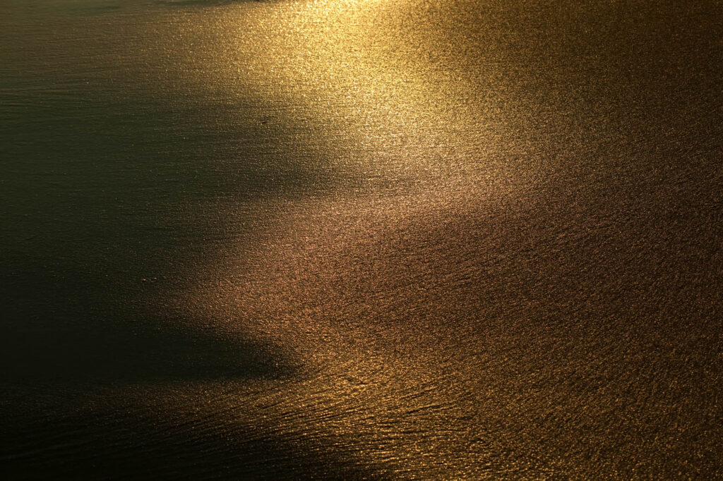 Złote światło wschodzącego słońca odbijające się od mokrej, teksturowanej powierzchni plaży | fot. Marcin Skrobisz