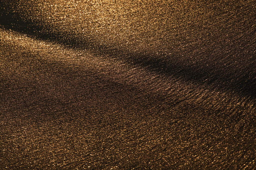 Zbliżenie na strukturę mokrego piasku podświetlonego promieniami zachodzącego słońca | fot. Marcin Skrobisz