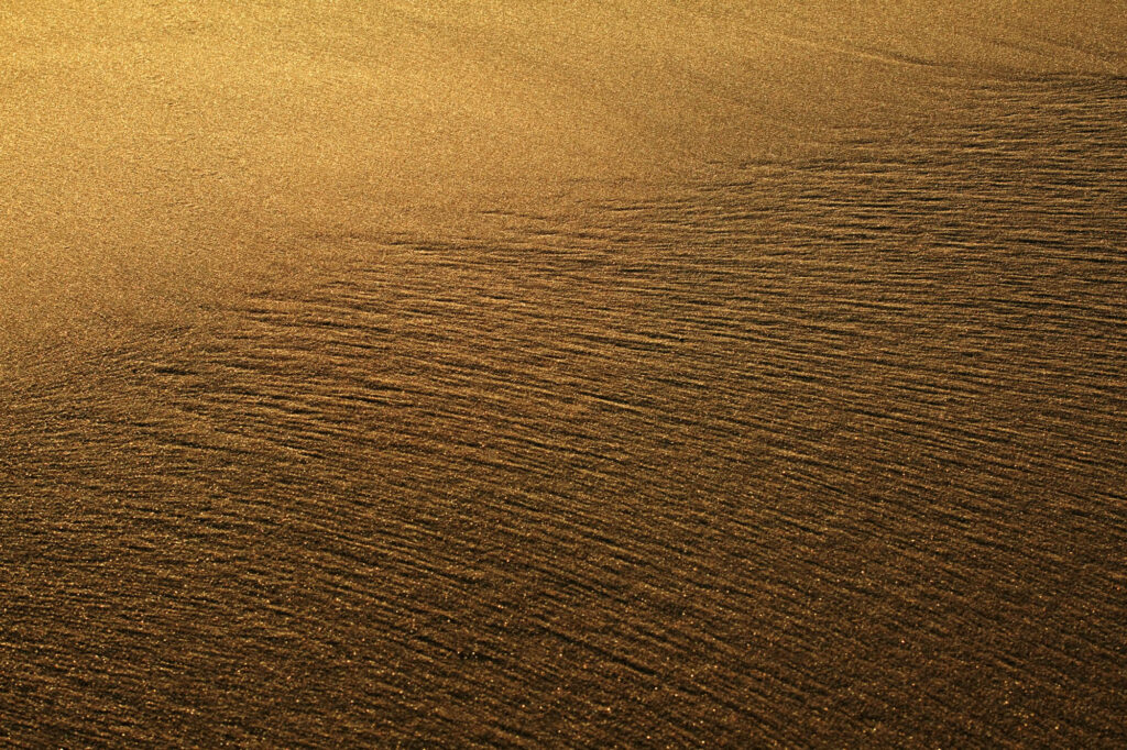 Struktura mokrego piasku na plaży oświetlonego niskim słońcem | fot. Marcin Skrobisz