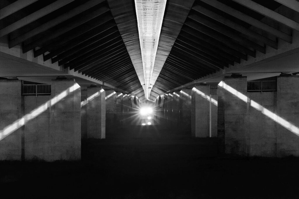 Czarno-białe zdjęcie pod betonowym mostem z promieniami światła tworzącymi geometryczny wzór | fot. Marcin Skrobisz