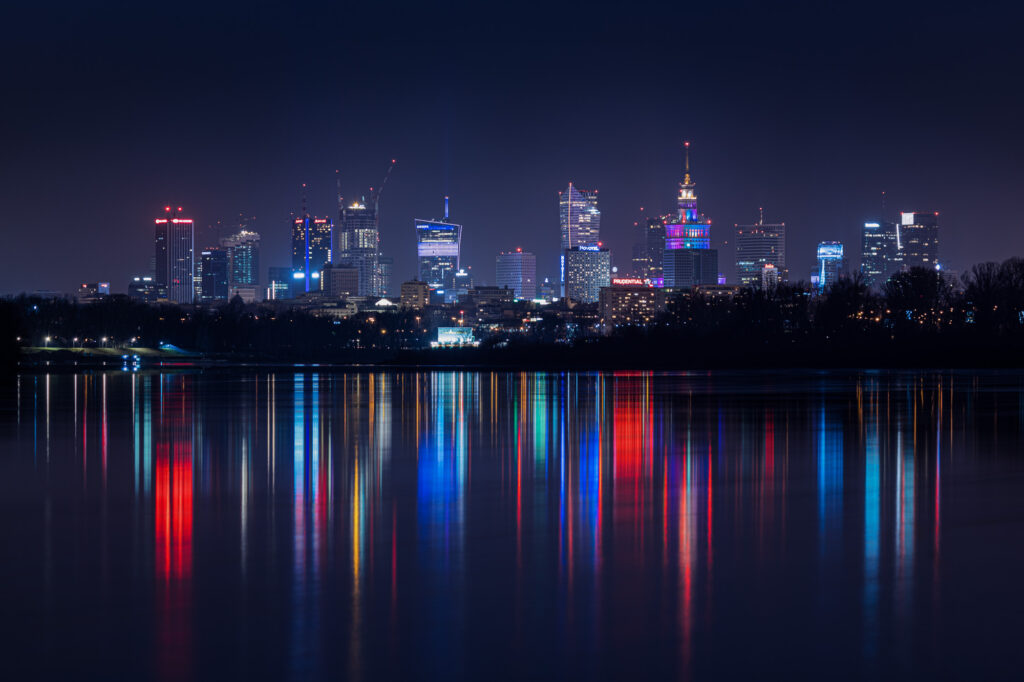 Nocna panorama Warszawy z kolorowymi odbiciami świateł wieżowców w Wiśle | fot. Marcin Skrobisz