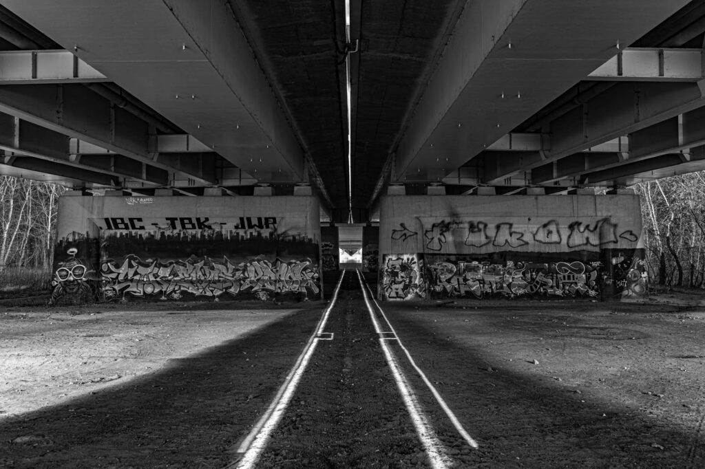 zarno-białe zdjęcie graffiti pod Mostem Siekierkowskim w Warszawie z promieniami światła przecinającymi ziemię | fot. Marcin Skrobisz