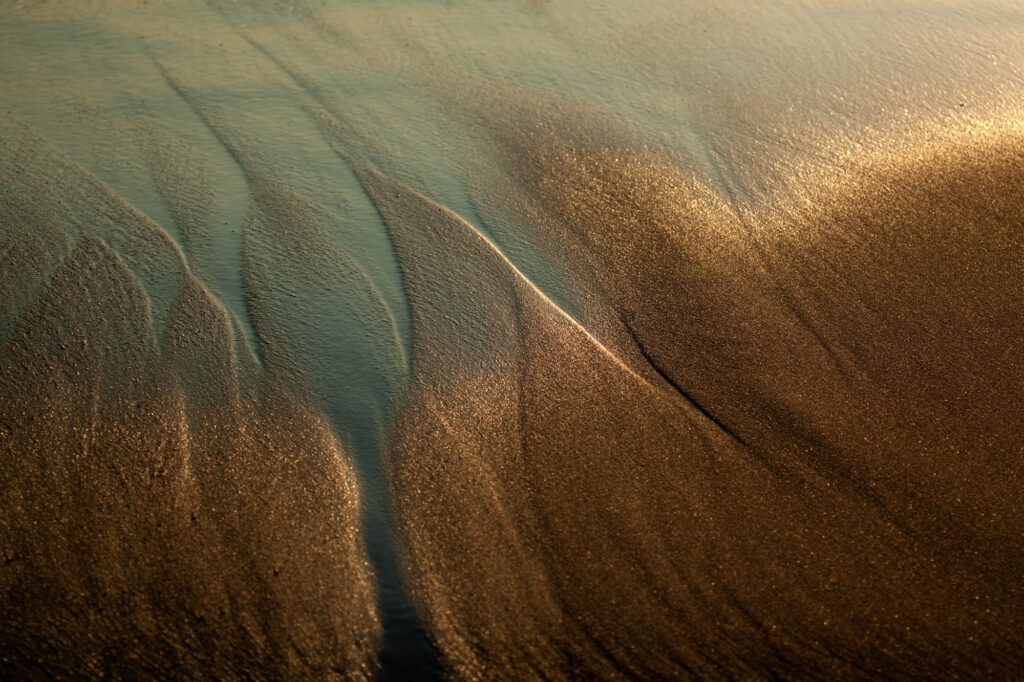 Złote struktury na wilgotnym piasku uformowane przez cofającą się wodę – subtelne światło wieczoru | fot. Marcin Skrobisz